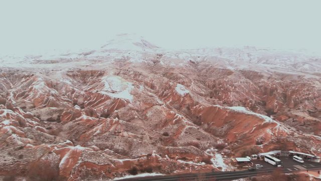 Cinematic aerial view of snowy landscape at Devrent Valley in Cappadocia. Fairy chimneys surronded by snow in Imaginary valley full of unique tuff rock formations in winter season in Cappadocia. 