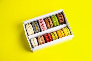 colorful macaroons in gift box for celebration romantic party birthday on yellow, pion flowers, satin ribbon top view, many different types flavors of macarons hand drawn decorated golden silver