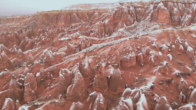 Cinematic aerial view of snowy landscape at Devrent Valley in Cappadocia. Fairy chimneys surronded by snow in Imaginary valley full of unique tuff rock formations in winter season in Cappadocia. 