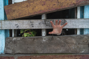 Frightening child in a terrible monster mask peeks extends a hand throung an old dirty window in village