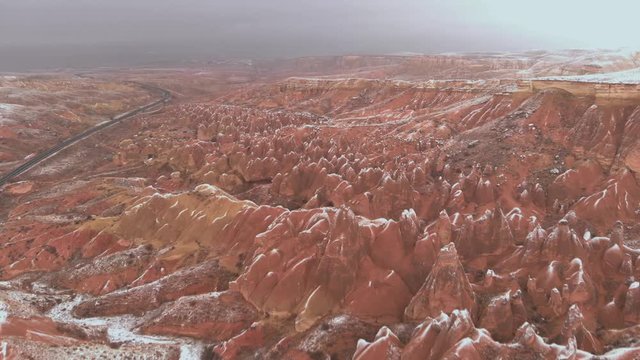 Cinematic aerial view of snowy landscape at Devrent Valley in Cappadocia. Fairy chimneys surronded by snow in Imaginary valley full of unique tuff rock formations in winter season in Cappadocia. 