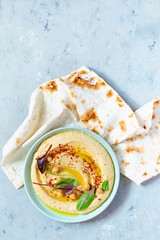 Classic hummus in a bowl with herbs, smoked paprika, olive oil and lettuce on a blue (gray) background. Healthy vegan food. A dish of Middle Eastern cuisine. Healthy eating concept.