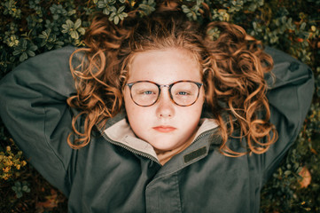 Portrait of pretty chubby girl with glasses lies on a grass