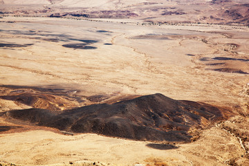 Fototapeta na wymiar A black hill among the orange desert consisting of black mineral. Scorched earth by the sun. View of the desert from above, panorama without horizon. Martian view