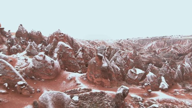 Cinematic aerial view of snowy landscape at Devrent Valley in Cappadocia. Fairy chimneys surronded by snow in Imaginary valley full of unique tuff rock formations in winter season in Cappadocia. 