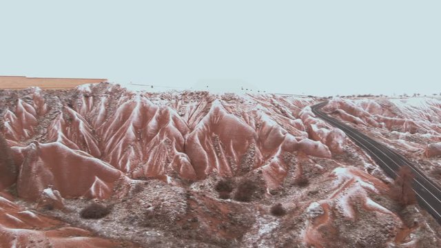 Cinematic aerial view of snowy landscape at Devrent Valley in Cappadocia. Fairy chimneys surronded by snow in Imaginary valley full of unique tuff rock formations in winter season in Cappadocia. 