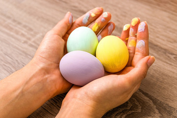 easter concept. closeup beautiful woman hands holding three eggs colored in tender pastel colors yellow, mint and purple over wooden table