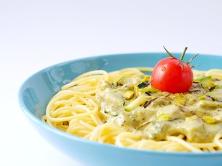 Spaghetti with a cream sauce with zucchini and leek with some tomatoes for decoration in a light blue plate on a white background from above.
