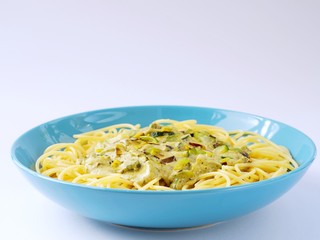 Spaghetti with a cream sauce with zucchini and leek in a light blue plate on a white background from above.