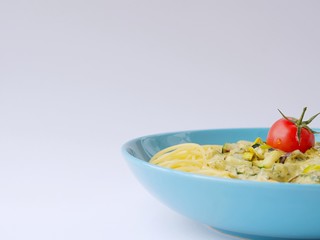 Spaghetti with a cream sauce with zucchini and leek with some tomatoes for decoration in a light blue plate on a white background from above.