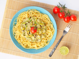 Spaghetti with a cream sauce with zucchini and leek with some tomatoes for decoration in a light blue plate on a white background from above.