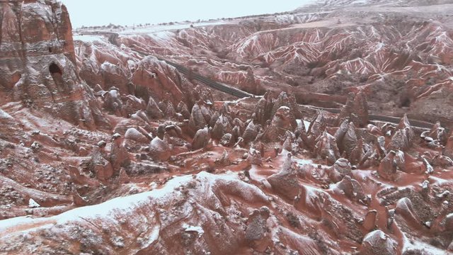Cinematic aerial view of snowy landscape at Devrent Valley in Cappadocia. Fairy chimneys surronded by snow in Imaginary valley full of unique tuff rock formations in winter season in Cappadocia. 