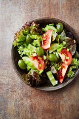 Healthy salad with green olives, cucumber and tomatoes. Rustic stone background. Top view.