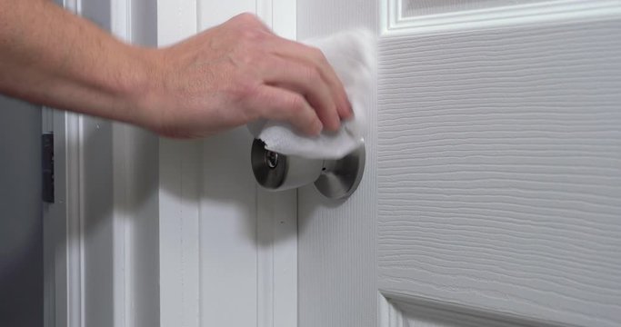A man sanitizes a doorknob with a disinfectant wipe before entering. Disinfecting and cleaning surfaces became a necessity during the coronavirus COVID-19 pandemic of 2020.  	