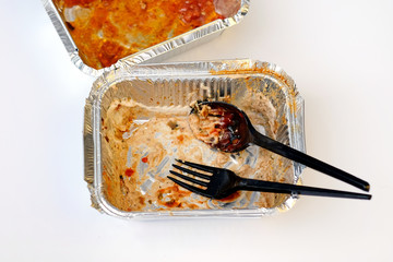 dirty empty aluminum container with black plastic spoon and fork top view. Food containers, disposable tableware after use. Home delivery food.