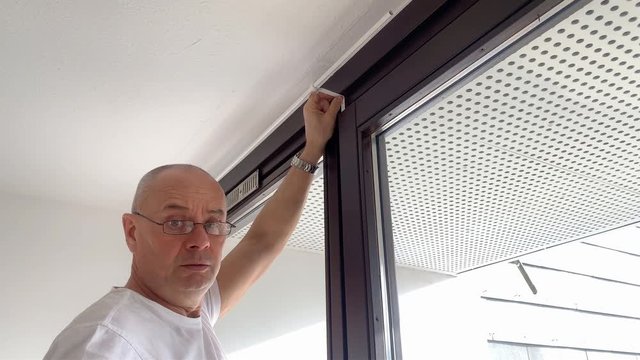 bald man in middle-aged glasses is twisting screws for cornices on the window in the room, the concept of male homework, repair, housewarming