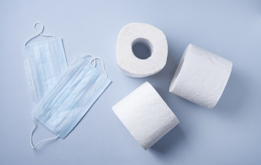 three rolls of white toilet paper and face masks on a blue background. Pandemic, covid-19, essential goods, scarcity