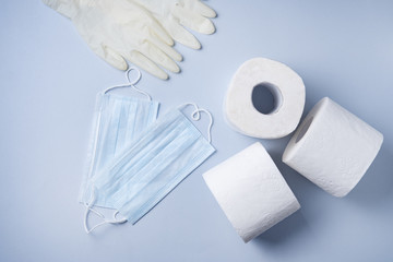 three rolls of white toilet paper, medicine gloves and face masks on a blue background. Pandemic, covid-19, essential goods, scarcity