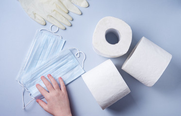 three rolls of toilet paper and madicine gloves and masks are taken by hand on a blue background. Pandemic, covid-19, essential goods, scarcity