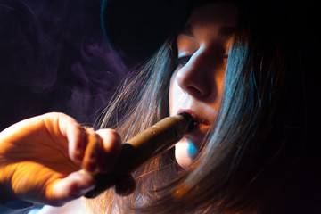 The concept of vaping. A long-haired girl enjoys Smoking an electronic cigarette. A woman in a...