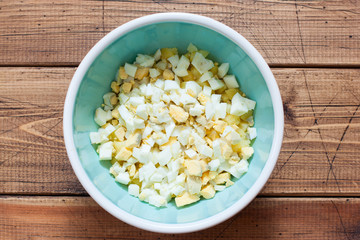 Step by step preparation of cold okroshka soup with sausage, step 3 - adding chopped chicken egg, top view, selective focus