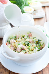 Traditional summer okroshka soup with sausage and vegetables in white miskes with added water, selective focus
