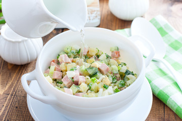 Traditional summer okroshka soup with sausage and vegetables in white miskes with added water,...