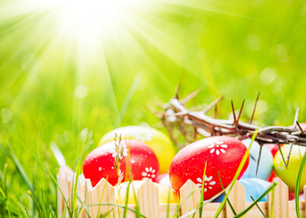 Crown of thorns and colorful eggs in green grass at sunny day. Easter background