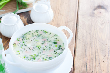 Traditional summer okroshka soup with sausage and vegetables in a white bowl, copy space