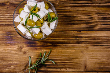 Chopped feta cheese, rosemary and olives in glass bowl on a wooden table. Top view