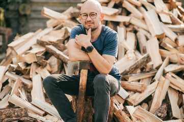 Picture of beautiful caucasian man stands with an axe against the background of a large pile of firewood