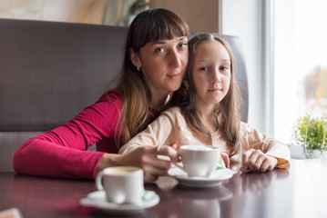 Mom and daughter are drinking coffee in a cafe. Photographed close-up.