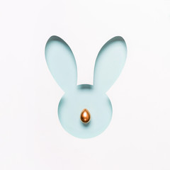 Hole Easter Bunny face made of cut paper and golden egg nose. Happy easter minimal concept in pastel colors