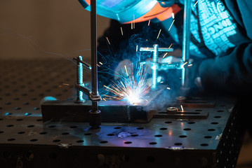 A welder works in a workshop and welds a metal pipe