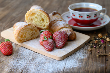 Tasty sliced croissant on a wooden board and a cup of tea