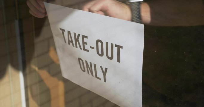 A cafe owner puts a TAKE OUT ONLY sign on the front door. Take out or carry away quickly became the only option for restaurants during the coronavirus COVID-19 pandemic of 2020.  	