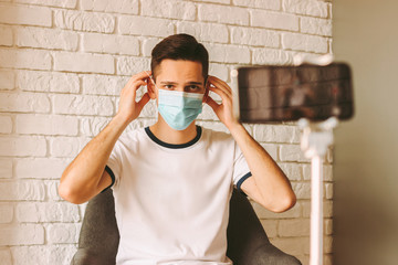 Young man in medical mask on face filming content for internet subscribers on smart phone camera....