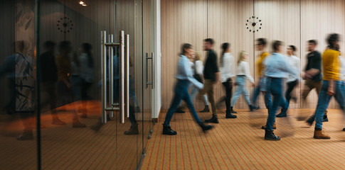 Group of office employees in motion go around at coworking space. People in business center walking...