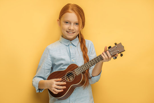 portrait of beautiful caucasian teen girl with natural red hair holding ukulele in hands, she enjoy playing in such unusual type of instruments ukulele, small guitar. music, people, children concept