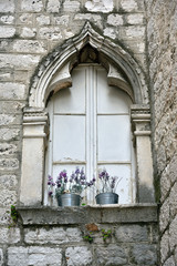 Fototapeta na wymiar A small flower pots in the decorated closed window in Sibenik old city, Dalmatia, Croatia