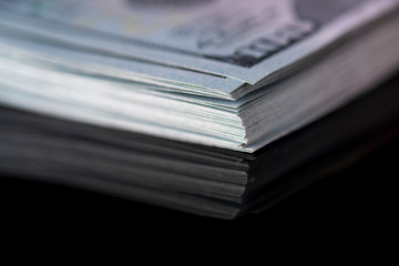 A stack of hundred dollar bills against a dark background. Photographed close-up.