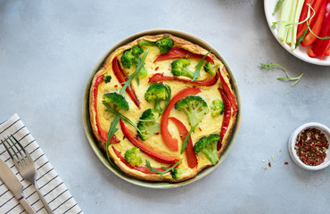 omelette or frittata with broccoli, bell pepper and arugula on a gray stone background. traditional italian dish. top view, horizontal image, copy space