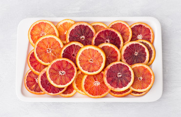 Sliced blood oranges circles on white plate on light background