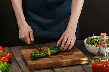 Woman cooking fresh healthy salad. Female hands cutting vegetables on board on wooden table.