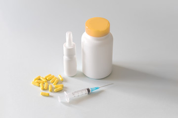 a jar of pills and yellow capsules with a syringe lie on a light background for an article on medicine