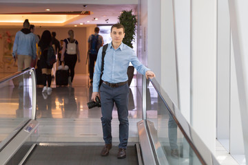 A man with a camera in his hand is among passers-by in a shopping business center.