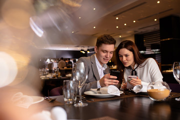 young caucasian couple have dinner together, look at smartphone in restaurant. guy show cool interesting video to girlfriend. indoors. man and woman enjoy spending time together