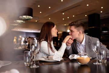 happy young caucasian couple spend their evening in restaurant, man adn woman on a date. lovely lady and handsome guy love each other, celebrate anniversary. gentleman kiss woman's hand