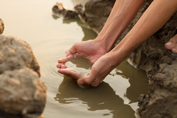 Hand taking water from dirty pond metaphor freshwater scarcity, drinking water and environment...