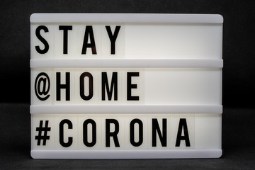 is written on an illuminated panel with black letters: Stay at home #Corona